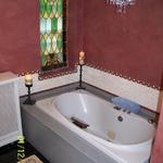 After picture of bathroom. We opened up the wall where the previous homeowner had dry-walled over the window. We also added an onyx mosaic tile 14" border around the tub. We applied a velvety venetian plaster to the walls, added an area rug, candelabra and stain glass panels.